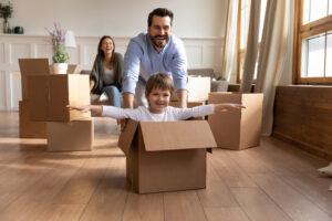 Family pushing a child around in a box after moving into a new home, possibly bought as a concessionary purchase
